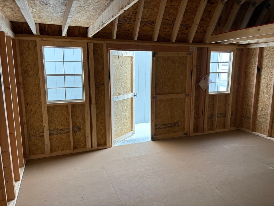 Interior of a lofted barn with the double shop doors open onto snow, two grid windows and open stud walls ready to finish