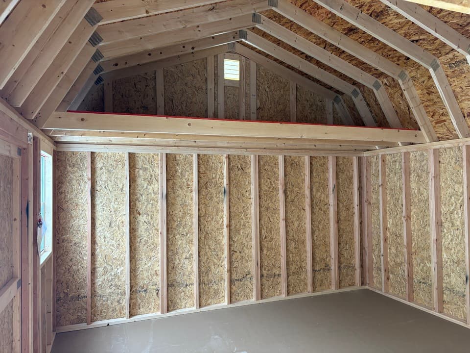 Interior of a side lofted barn showing the full-width overhead storage loft, exposed roof framing and unfinished OSB walls