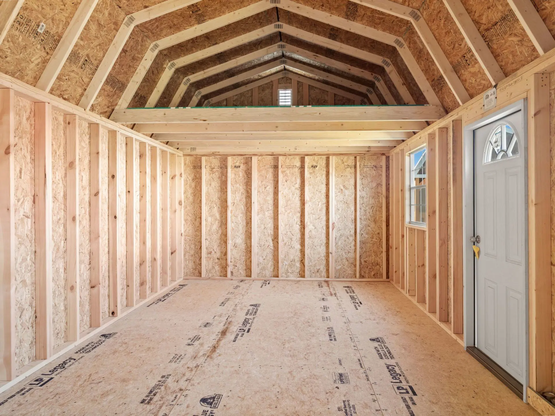Unfinished interior of a Stor-Mor lofted garage: bare stud walls, exposed barn-style roof framing, a storage loft across the back and a white entry door on the right