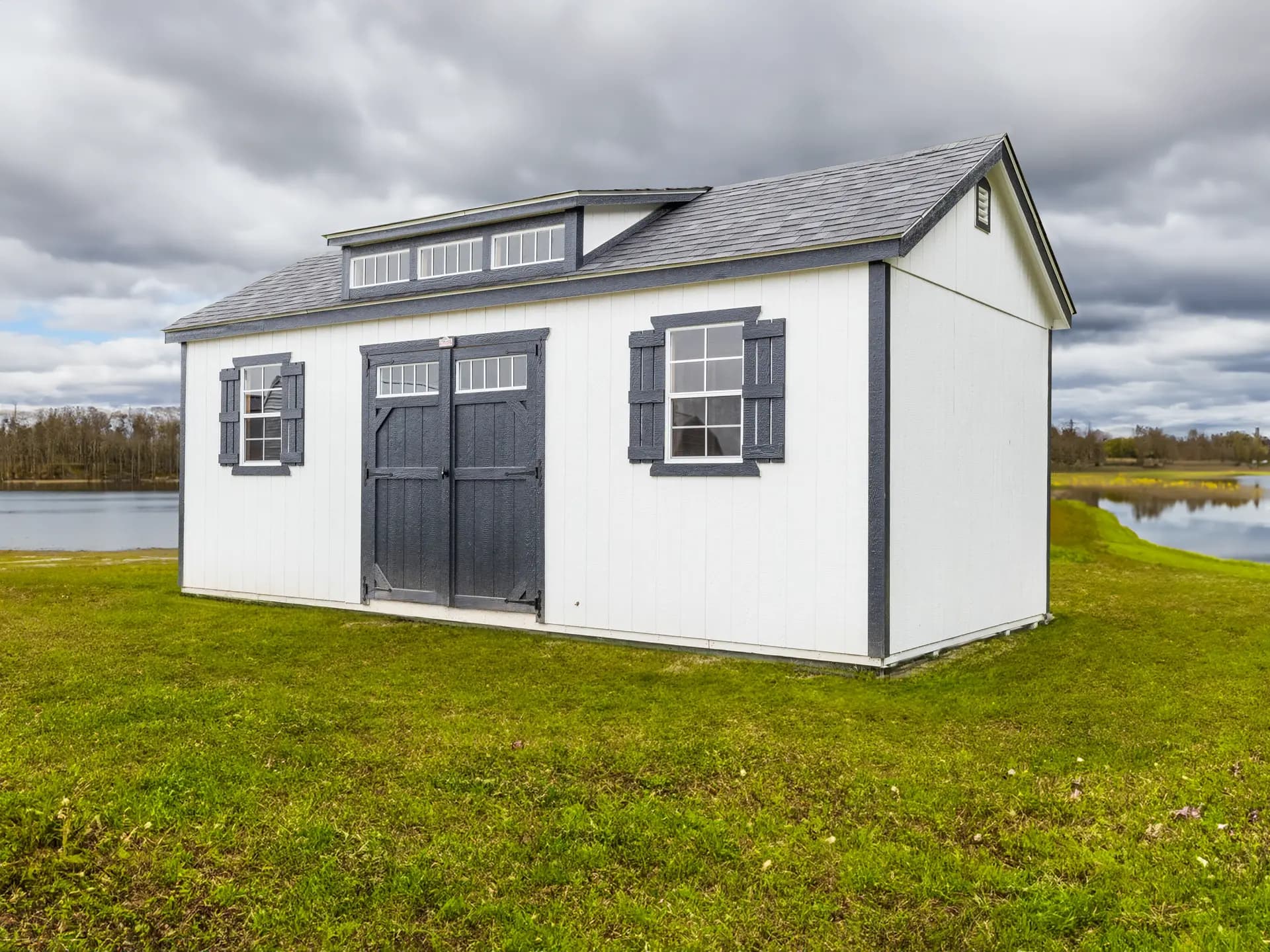 Stor-Mor 12x24 side utility shed in white with charcoal trim, window shutters and a transom roof dormer, doors set in the long side wall